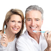 An older couple smiling and holding toothbrushes.