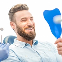 Man smiling at his reflection in dentist's mirror