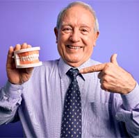 Man with dentures in Covington holding a model of teeth