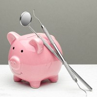 Dental tools leaning next to a large pink piggy bank