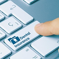 A finger pressing a ‘Dental Insurance’ key on a keyboard