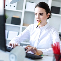 Young woman with dental implants in Covington, GA typing and holding pen in mouth