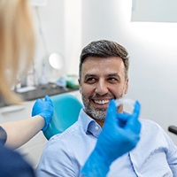 Male patient smiling at dental assistant holding Invisalign aligner