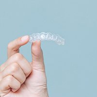 Closeup of patient holding Invisalign aligner against blue background