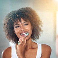 Woman in white shirt smiling while brushing her teeth