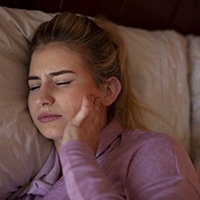 Woman in bed, suffering symptoms of TMJ disorder