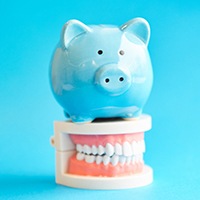 Piggy bank atop model teeth representing the cost of veneers in Covington 