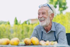 a man smiling with dental implants while sitting in front of healthy foods