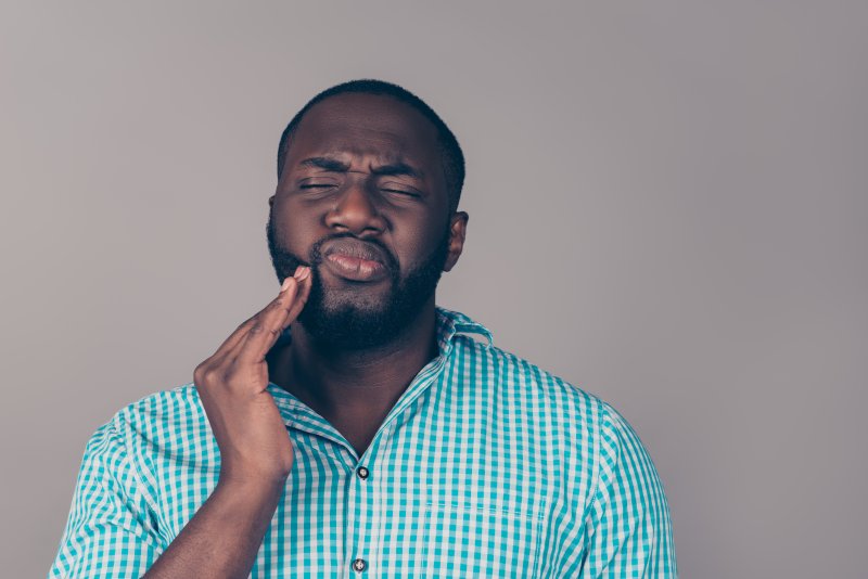 Man holding hand up to face, massaging cheek, and grimacing