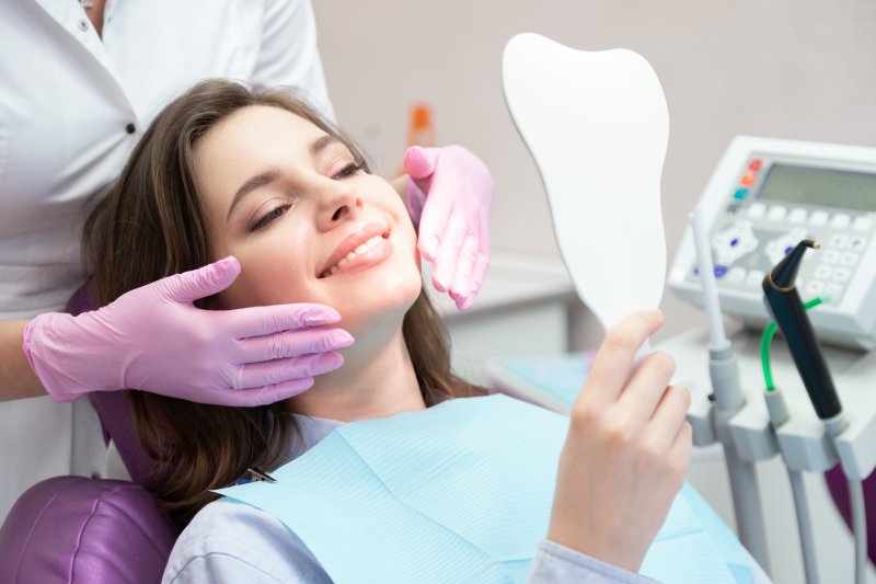A woman looking at her teeth in the mirror after a dental screening and cleaning
