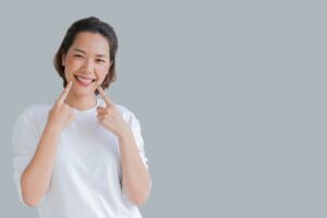 Woman in white shirt with gray nails pointing to her smile. 