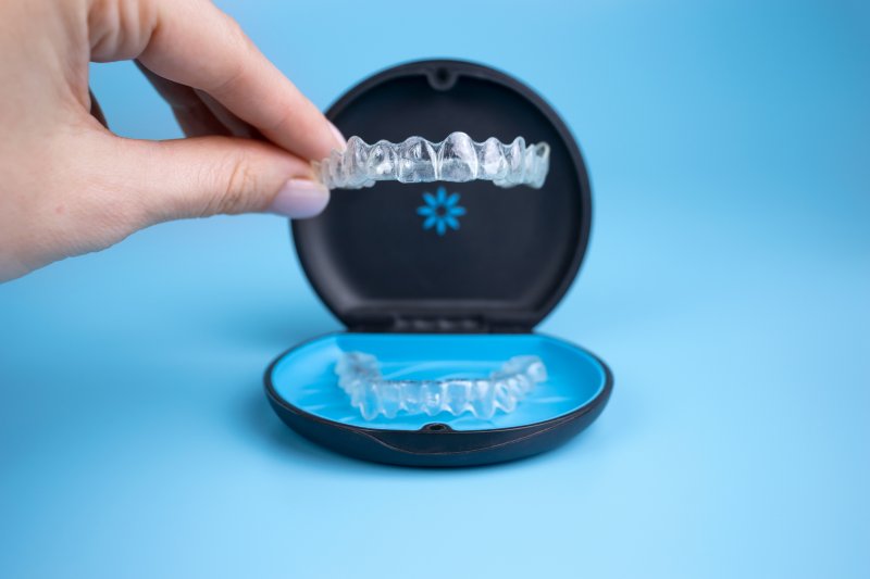 A hand holding an Invisalign aligner with a box on the table